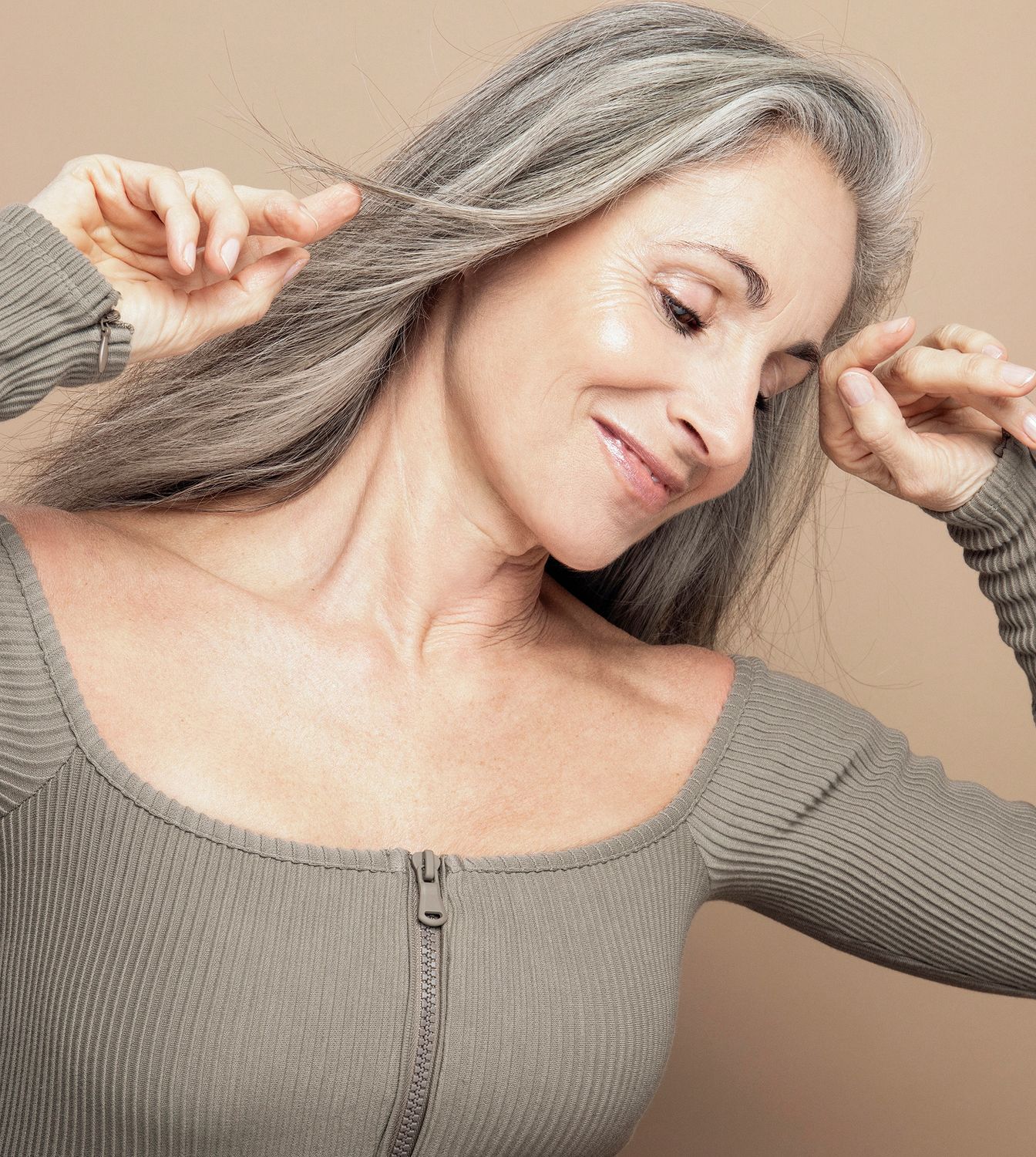 Woman with gray hair smiling and styling hair.